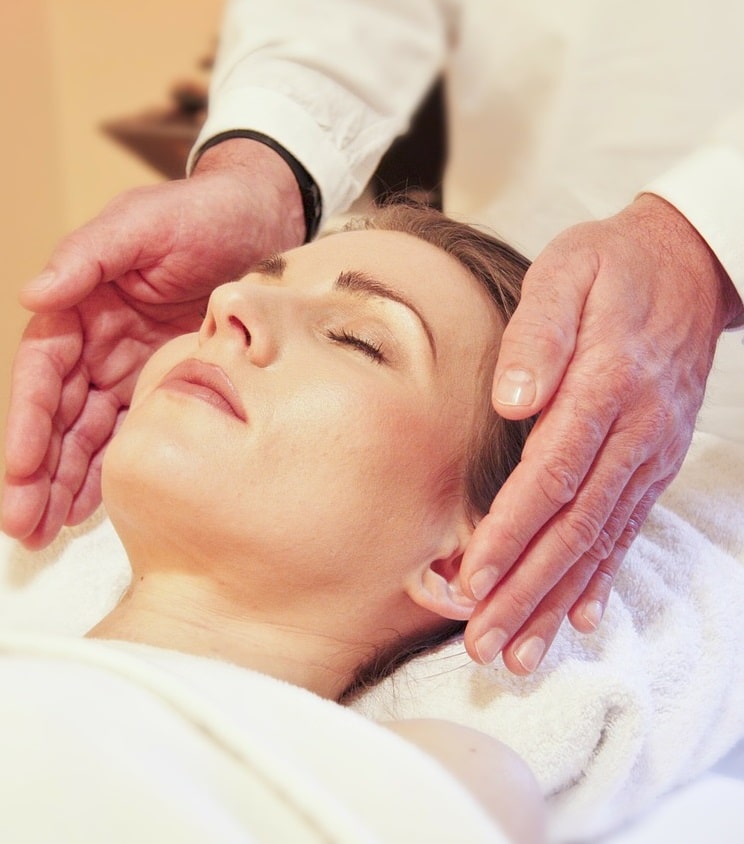 A woman lying down while a reiki healer has his hands around her head