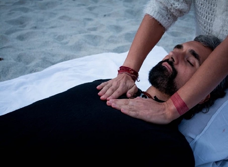 A man lying down while a healer has her hands on his chest