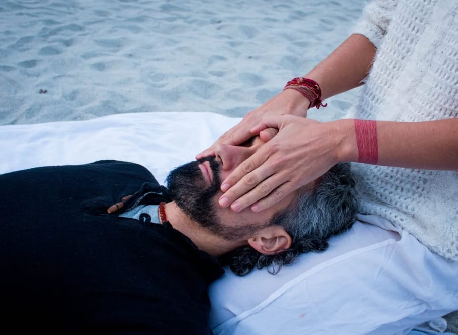 A man lying down while a healer has her hands on his face